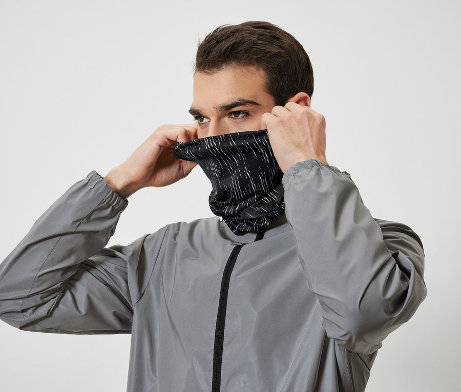 Un homme enfile un cache-cou noir rayé blanc et porte une veste grise.