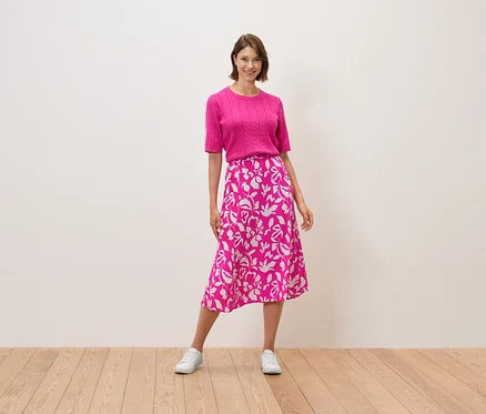 Une femme debout portant un haut rose et une jupe à motifs floraux.