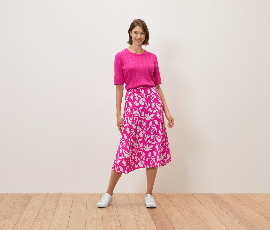 Une femme debout portant un haut rose et une jupe à motifs floraux.