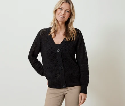 Une femme porte un cardigan en maille pointelle noir et un pantalon beige.
