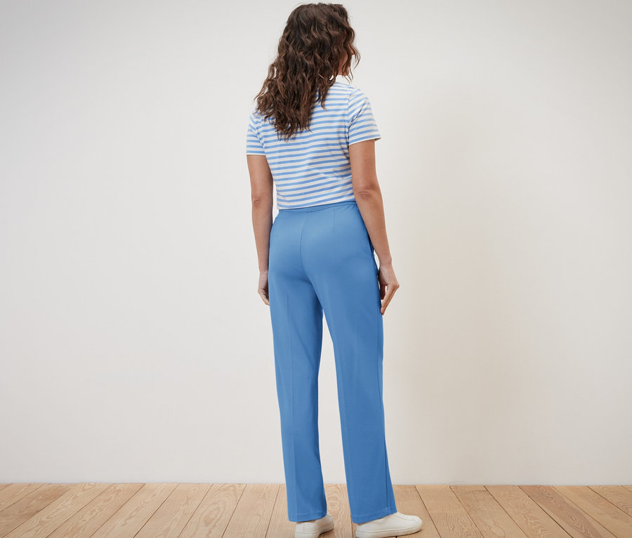 Femme vue de dos portant un pantalon en jersey bleu avec passepoil et un t-shirt rayé.