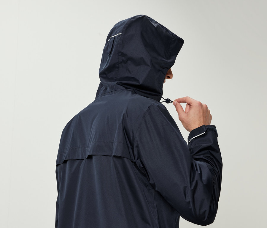 Un homme en veste de pluie bleu marine avec une capuche serre le cordon de la capuche.