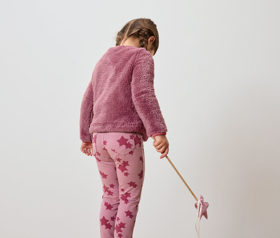Fillette portant un pull rose et un pantalon à motifs étoilés tenant un bâton avec une étoile.
