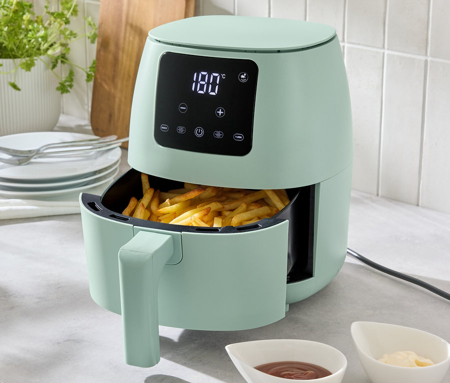 Une friteuse à air chaud vert clair de 2 l est posée sur un comptoir de cuisine, remplie de frites. Deux petits bols de sauces sont placés devant.