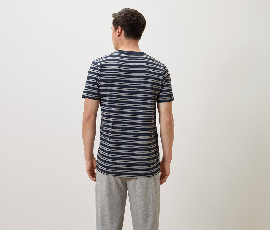 Un homme vu de dos portant un t-shirt rayé bleu et gris et un pantalon de jogging gris.