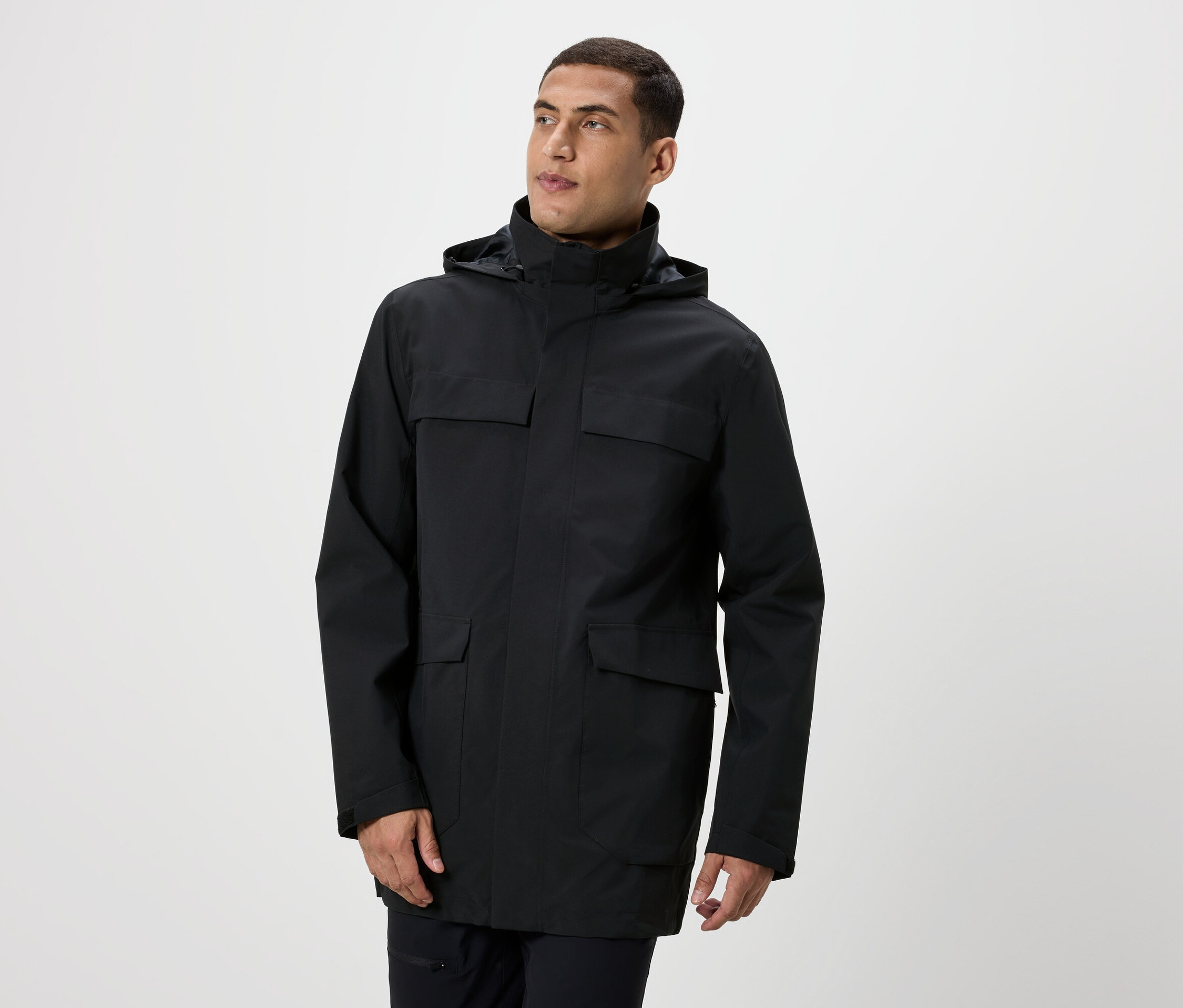 Un homme pose en veste noire à capuche avec des poches.