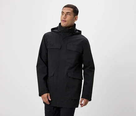 Un homme pose en veste noire à capuche avec des poches.
