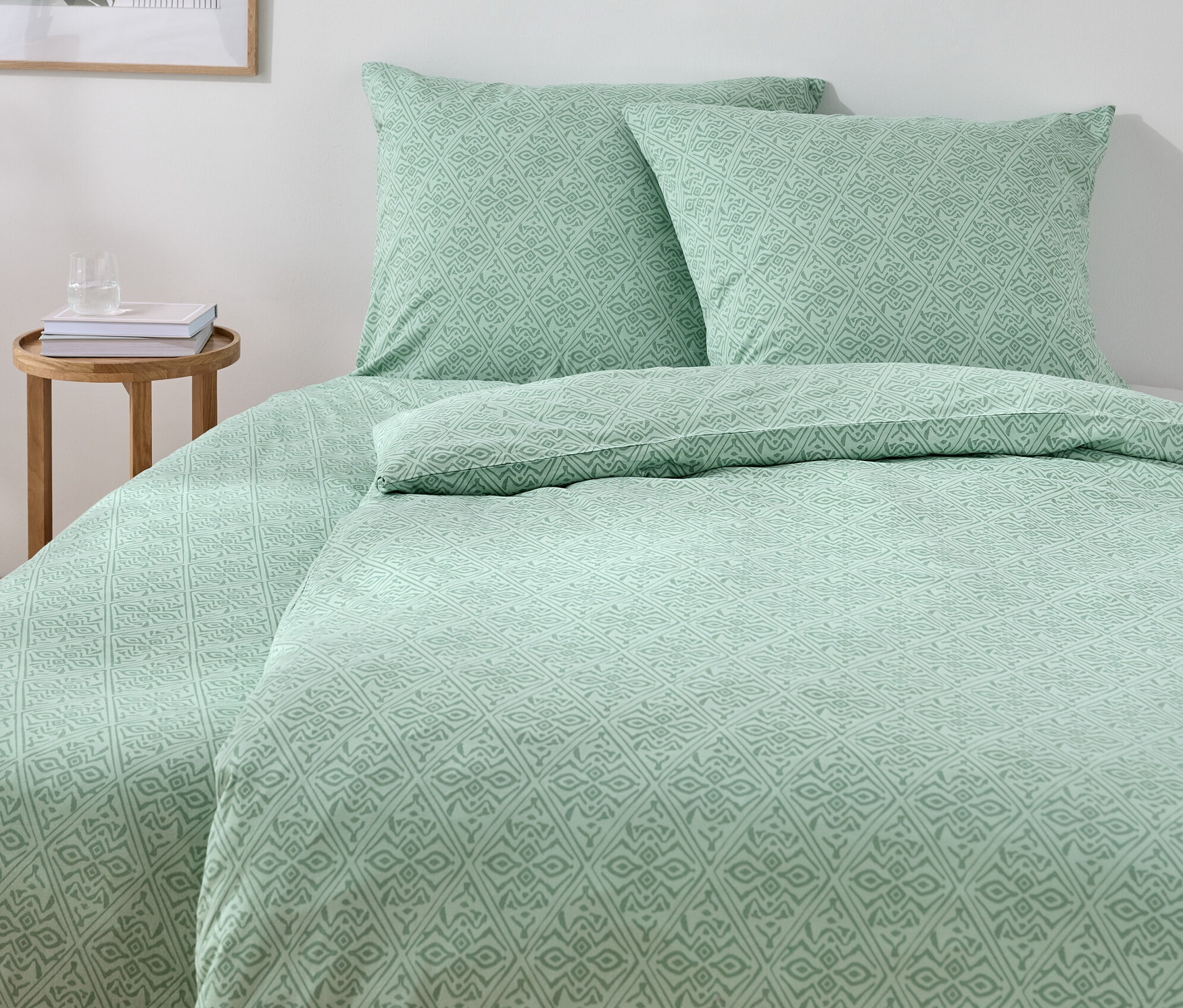 Parure de lit en jersey verte de taille standard et grande taille sur un lit avec deux oreillers et une table en bois.