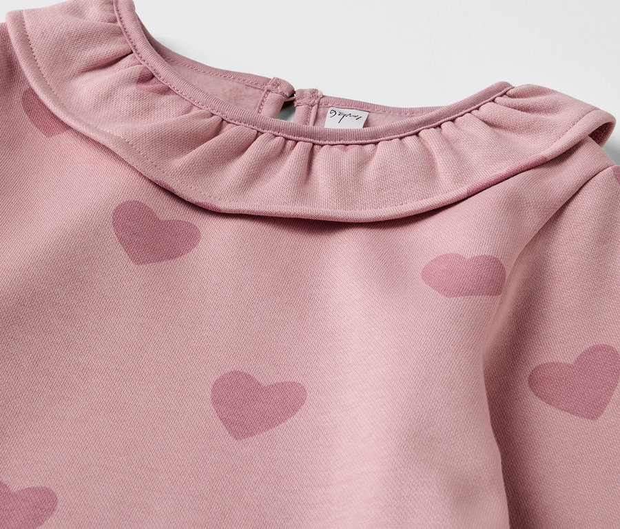 Détail d'une robe en sweat pour enfant avec un col à volants et un imprimé de cœurs.
