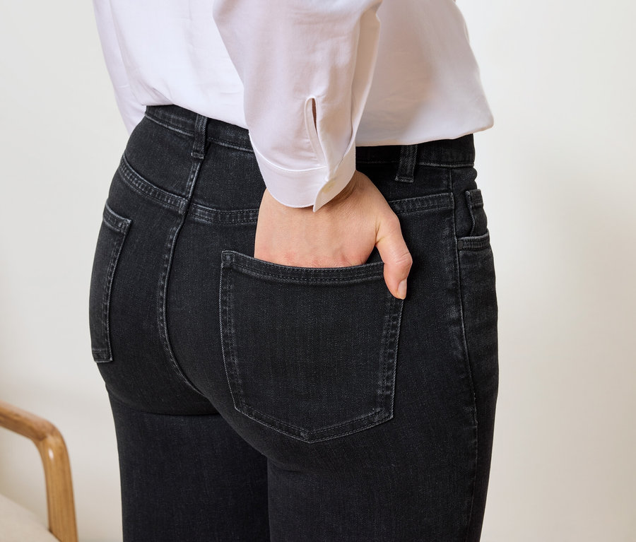 Gros plan d'une femme avec la main dans la poche d'un jean noir et une chemise blanche.