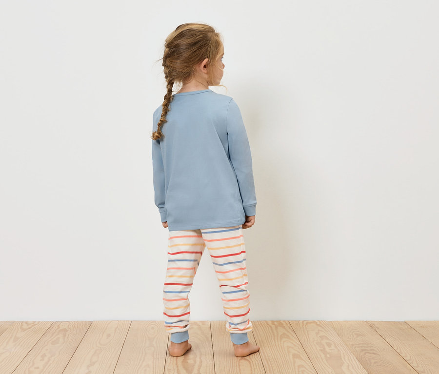 Fillette portant un haut bleu et un pantalon rayé, dos à la caméra.
