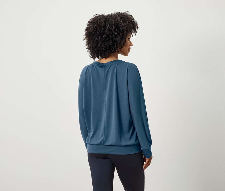 Vue arrière d'une femme avec une coiffure afro portant un haut bleu à manches longues et un pantalon bleu foncé.