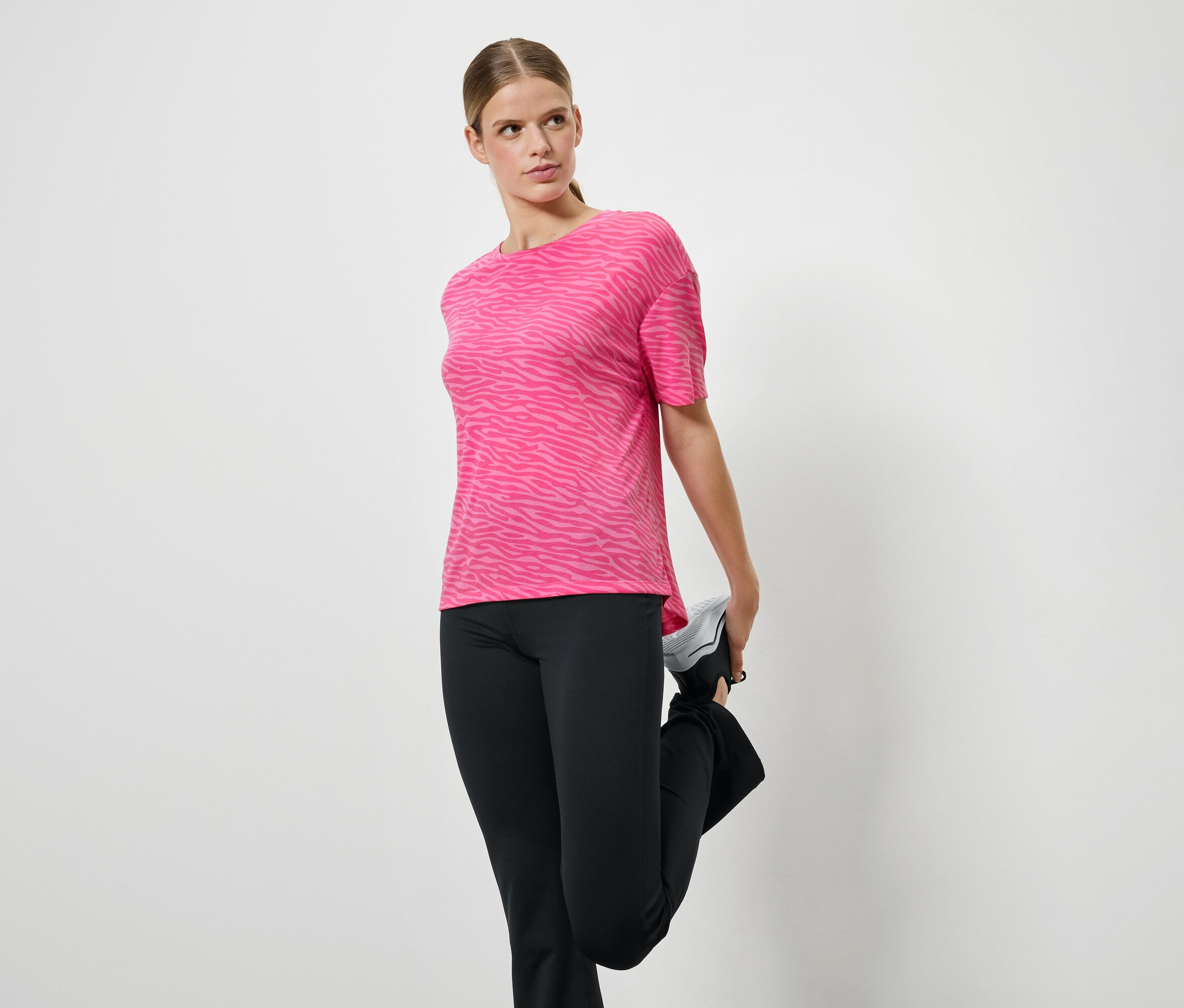 Femme étirant sa jambe en t-shirt de sport rose et pantalon noir.