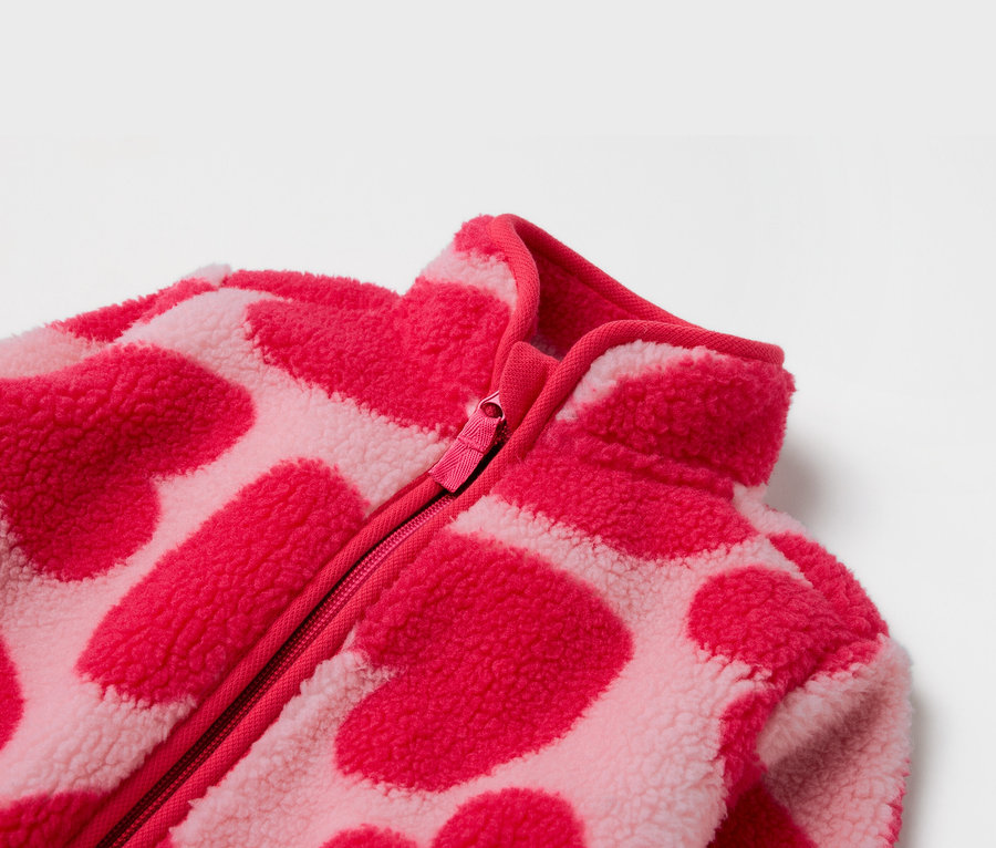 Détail d'une veste polaire rose avec fermeture éclair et motif de cœurs.