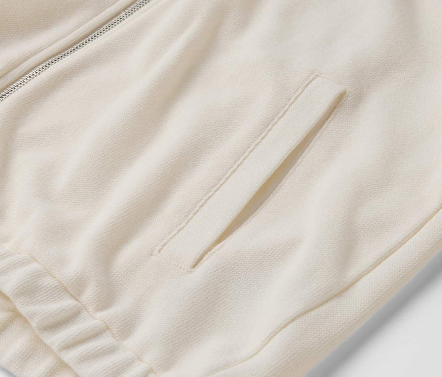 Gros plan sur un sweat zippé couleur crème avec une poche.