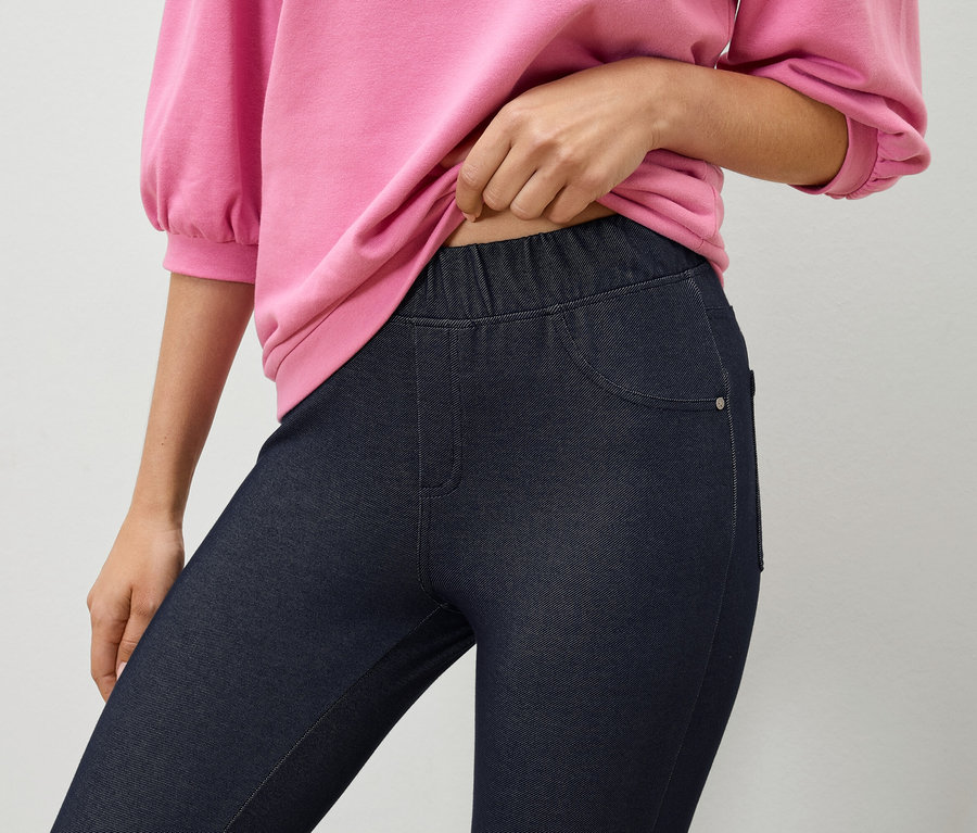Une femme tient un sweat-shirt rose au-dessus d'un jegging bleu marine.