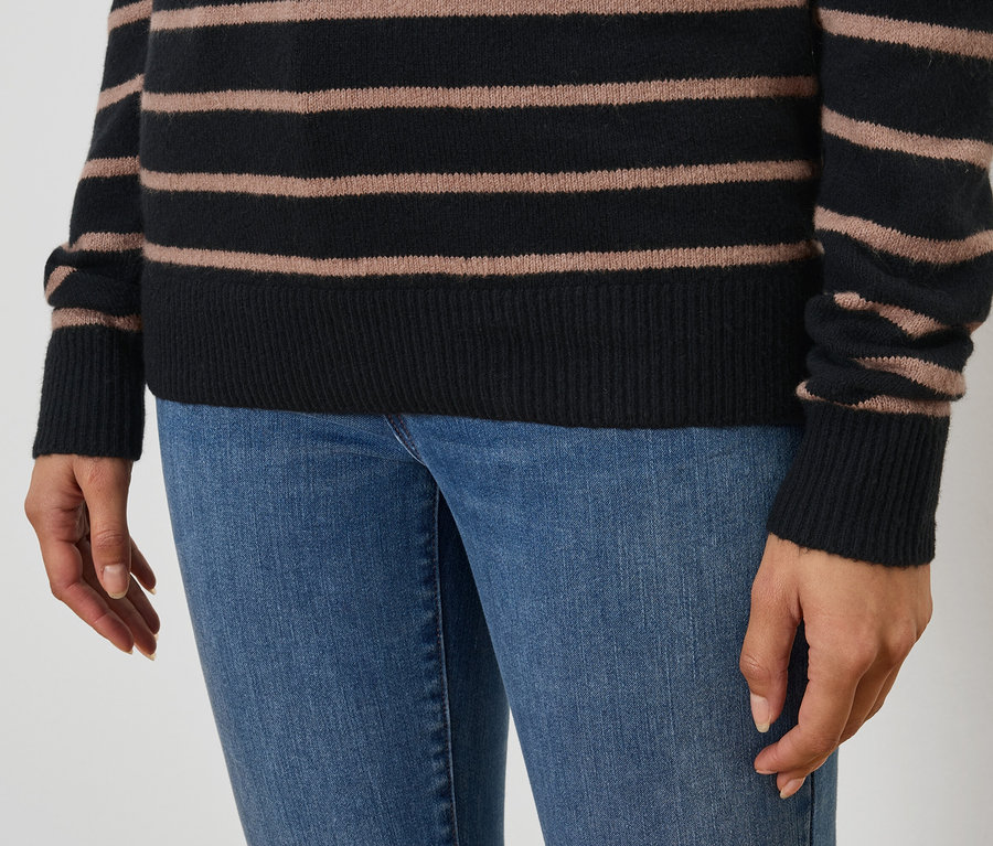 Gros plan d'une femme portant un pull rayé noir et marron et un jean bleu.