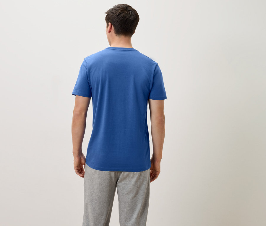 Vue arrière d'un homme portant un t-shirt bleu et un pantalon de survêtement gris sur un fond neutre.