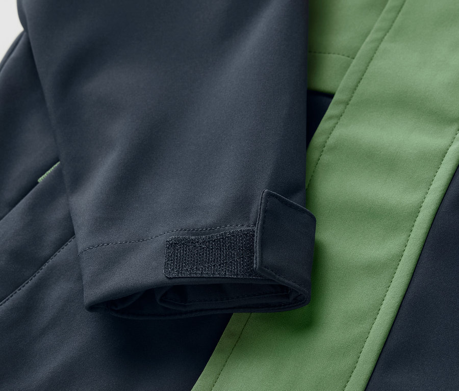 Gros plan sur une veste en softshell pour enfant bleu et verte avec une fermeture Velcro sur la manche.