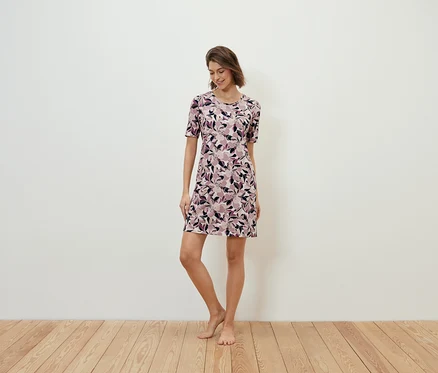 Une femme debout sur un plancher en bois porte une robe à fleurs.