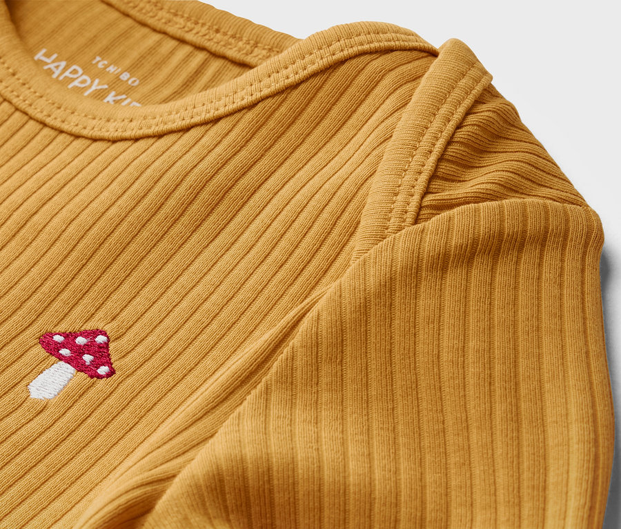 Gros plan sur un t-shirt jaune à manches longues pour bébé avec une texture côtelée et une broderie de champignon.