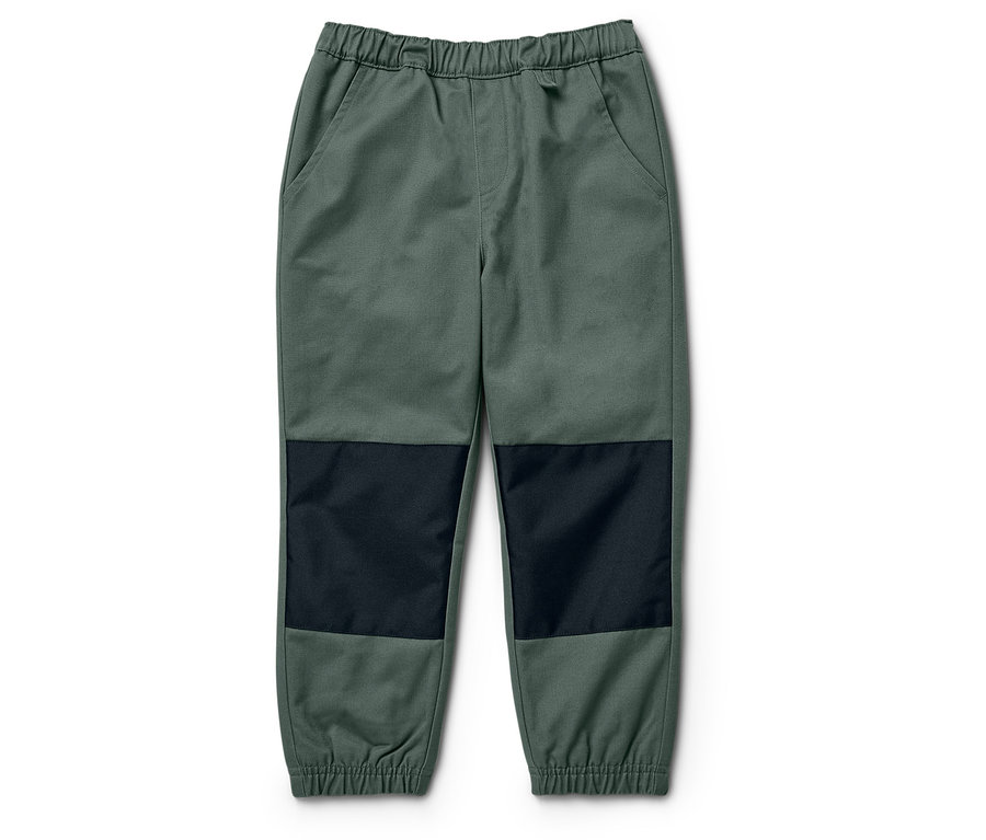 Un pantalon vert avec des pièces aux genoux noires posé sur un fond blanc.