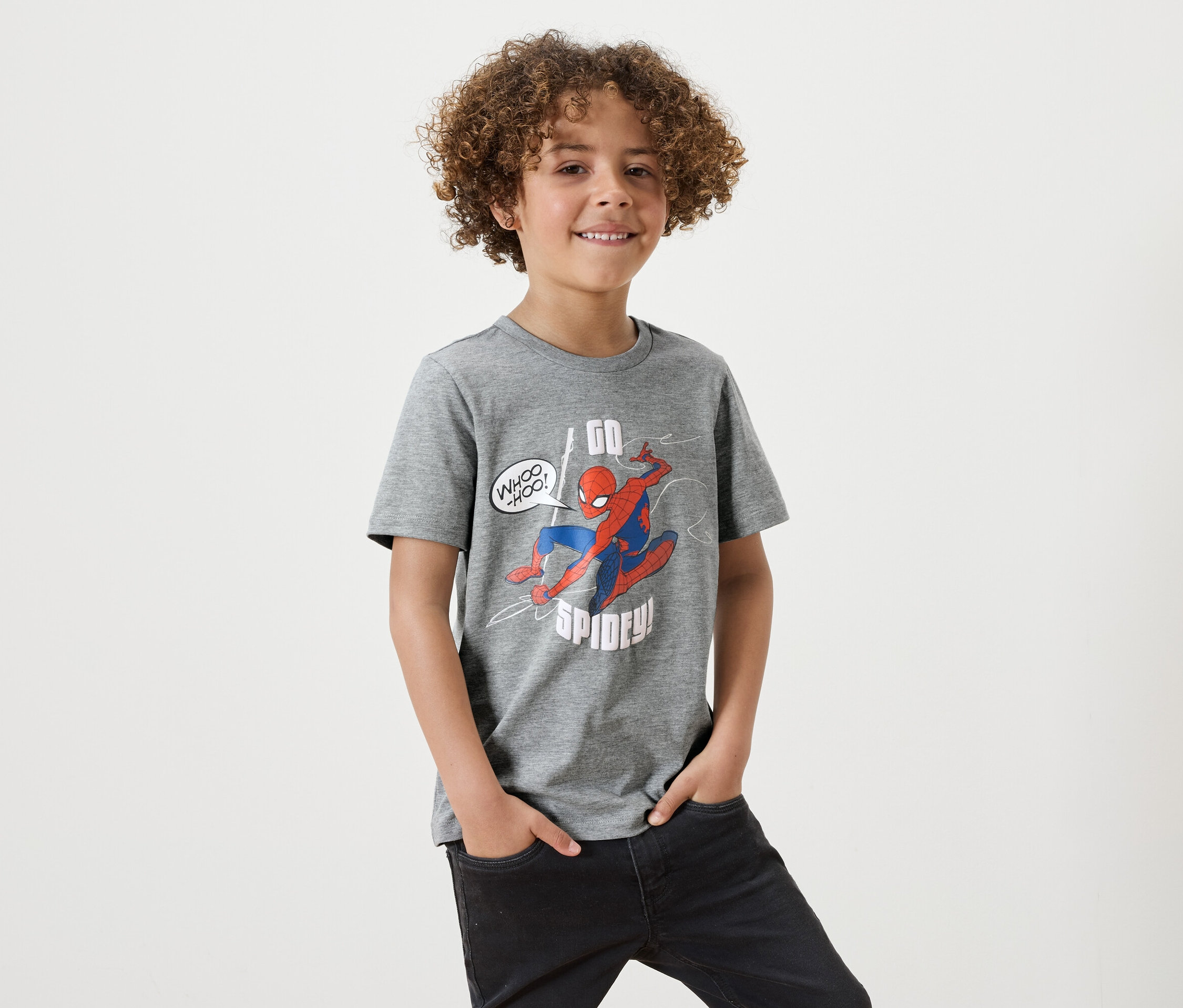 Un garçon aux cheveux bouclés porte un t-shirt gris avec un imprimé Spiderman.