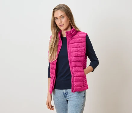 Femme portant un gilet matelassé rose sur un haut à manches longues bleu marine et un jean.