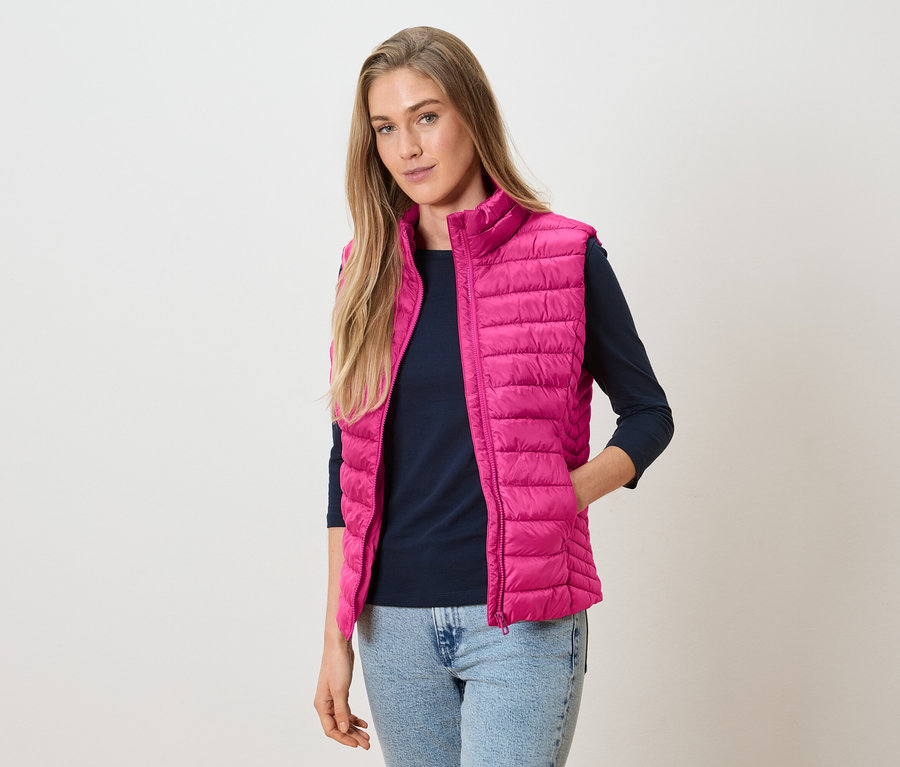 Femme portant un gilet matelassé rose sur un haut à manches longues bleu marine et un jean.
