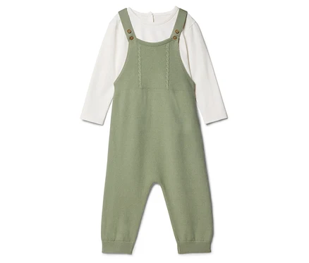 Une salopette verte en tricot pour bébé est posée sur un t-shirt blanc à manches longues.