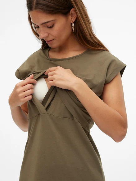 Une femme soulève sa robe d'allaitement vert olive pour révéler un soutien-gorge blanc en dessous.
