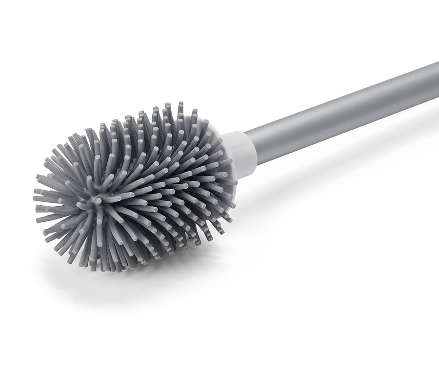 Une brosse de toilette grise avec un manche argenté est disposée en diagonale sur un fond blanc.