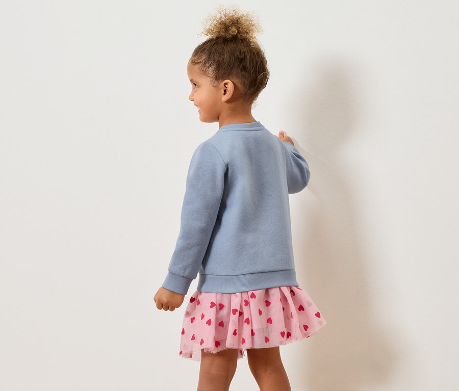 Fillette vue de dos portant un pull bleu et une jupe rose à cœurs.