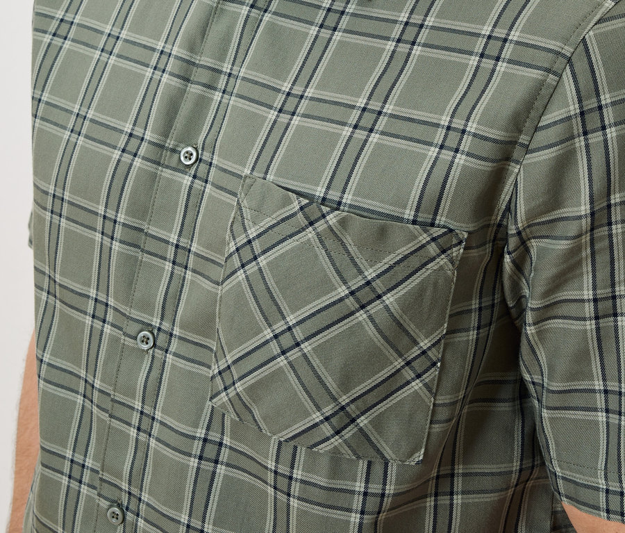 Gros plan d'une chemise à carreaux vert olive avec une patte de boutonnage et une poche poitrine.
