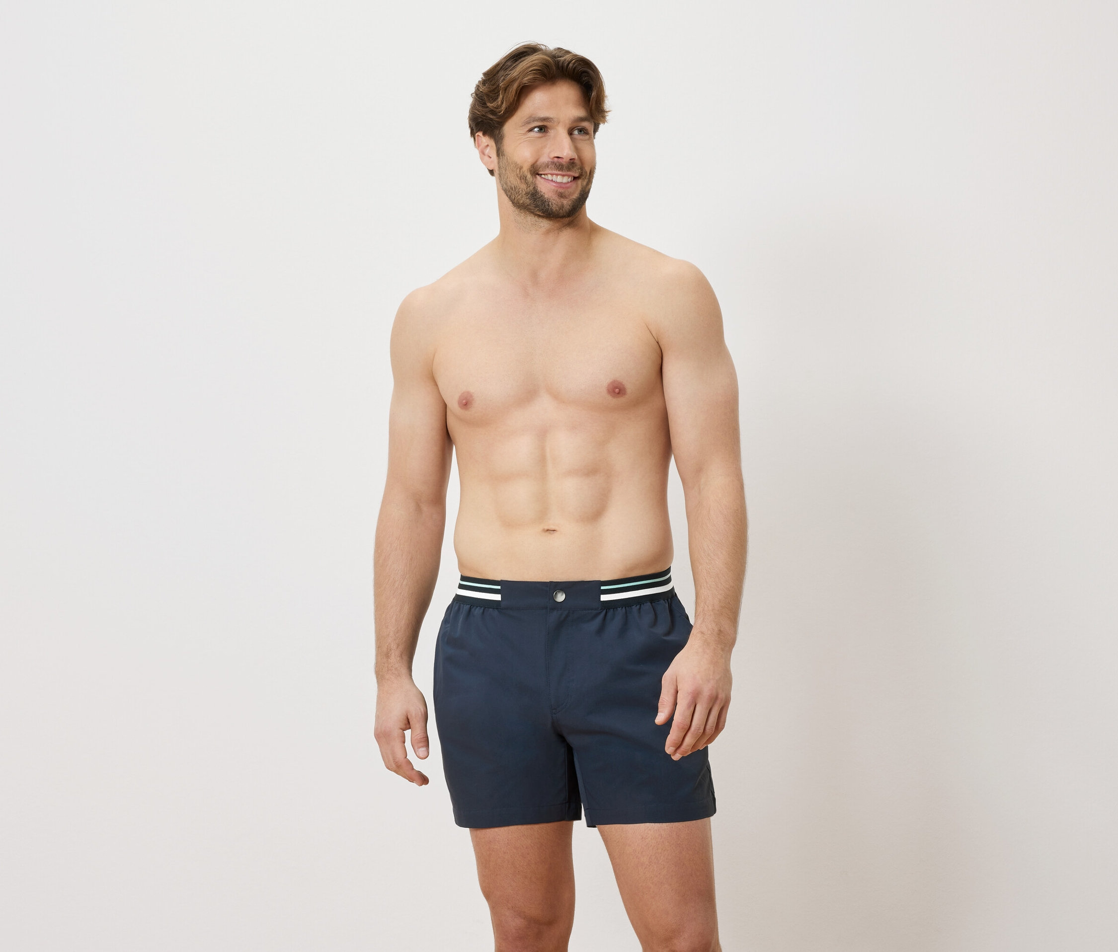 Un homme torse nu porte un caleçon boxer bleu avec une ceinture blanche et verte sur fond blanc.