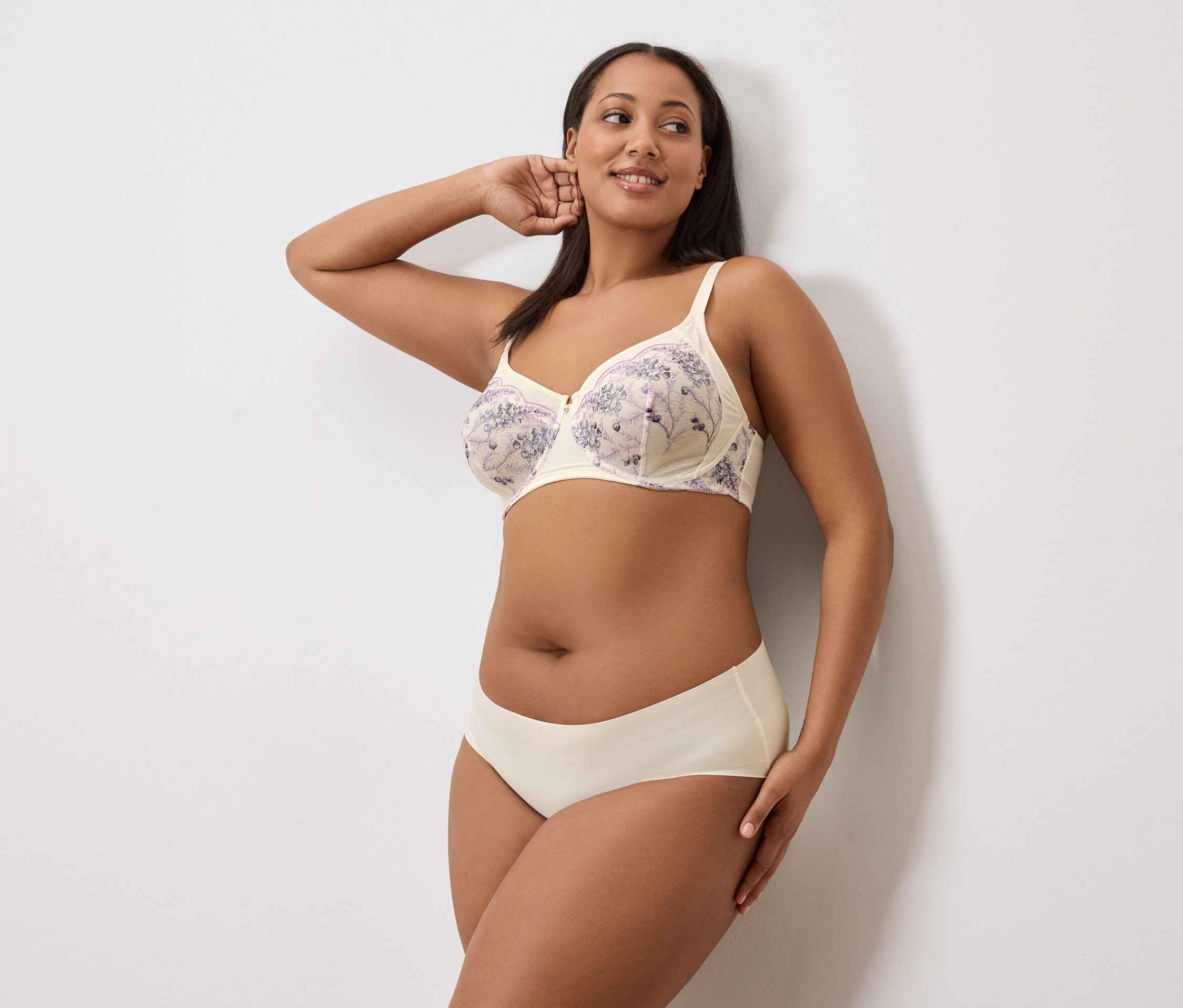 Une femme pose en soutien-gorge et culotte sur un fond blanc.