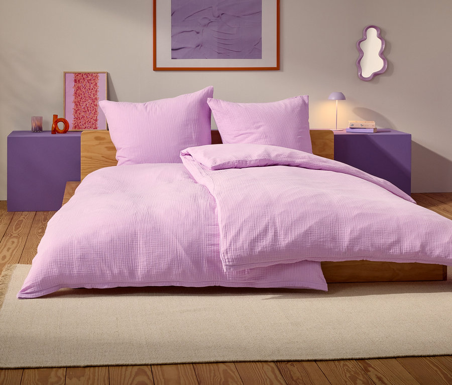 Un lit violet avec deux oreillers et une couverture se trouve sur un tapis beige dans une chambre.