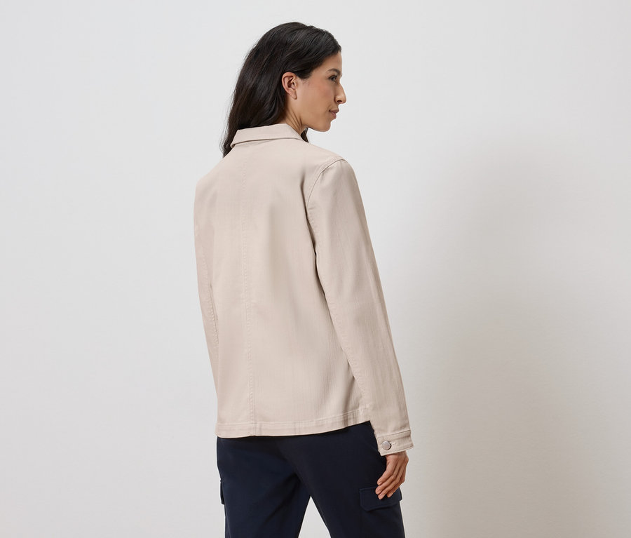 Femme vue de dos portant une veste beige et un pantalon bleu.