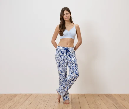 Une femme portant un soutien-gorge bleu clair et un pantalon de pyjama à motifs bleus et blancs se tient devant un mur blanc.