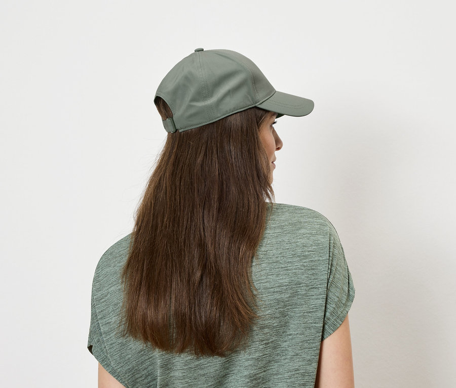Vue arrière d'une femme aux longs cheveux bruns portant un haut vert et une casquette verte.