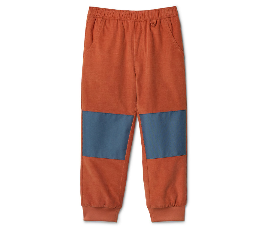 Pantalon en velours côtelé orange avec des pièces aux genoux bleues posé sur un fond blanc.