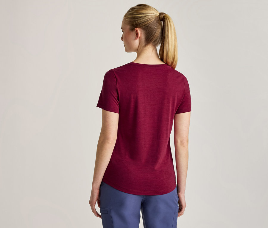 Une femme vue de dos, portant un t-shirt bordeaux à manches courtes et un pantalon bleu. Ses cheveux blonds sont attachés en queue de cheval.