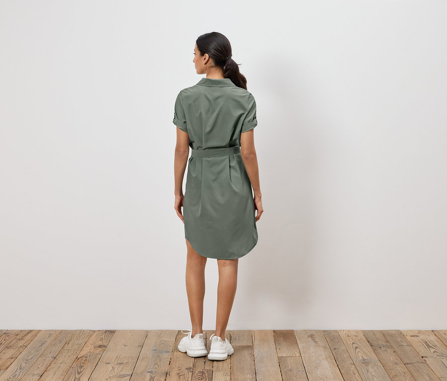 Une femme, dos à la caméra, porte une robe chemise vert olive avec une ceinture et des baskets blanches.