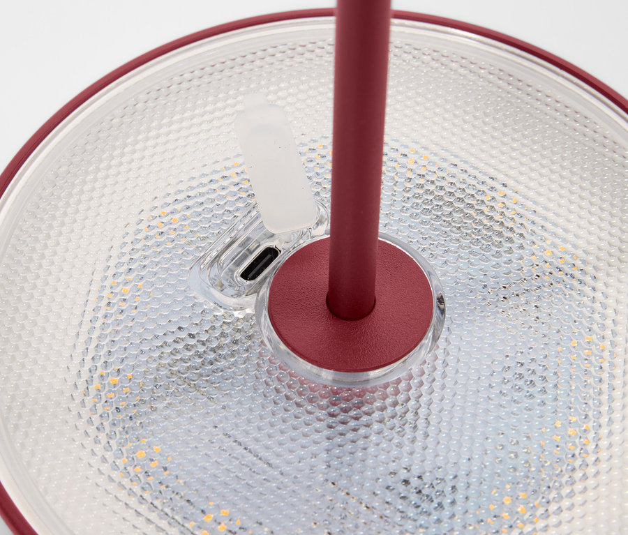 Gros plan d'une lampe avec bord rouge et support posée sur une surface texturée.