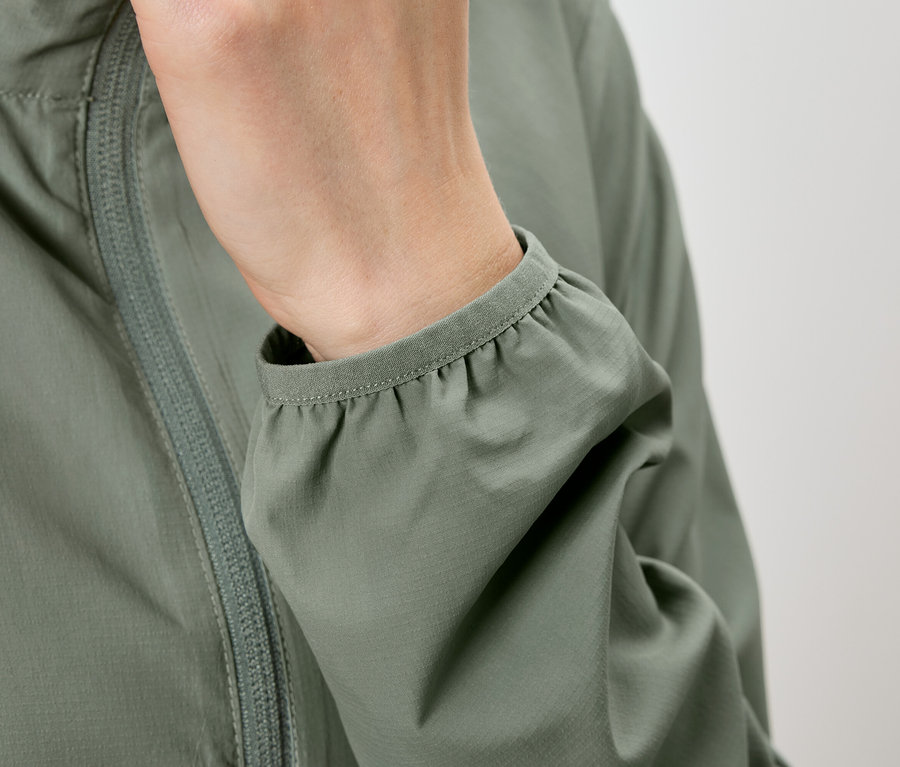 Gros plan d'une personne portant une veste vert olive, avec la main dans la poche et la manche froncée.