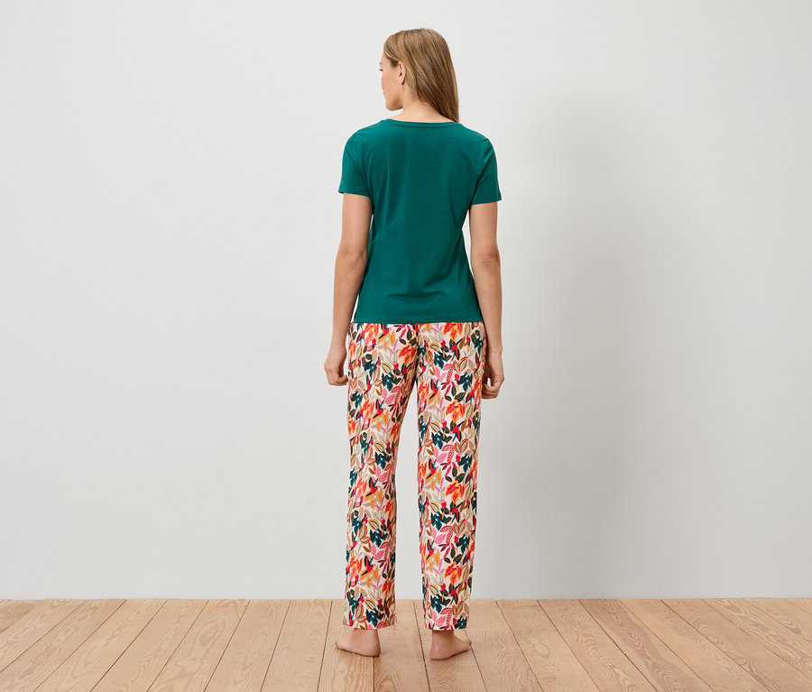 Vue de dos d'une femme blonde portant un t-shirt vert et un pantalon à motifs colorés.