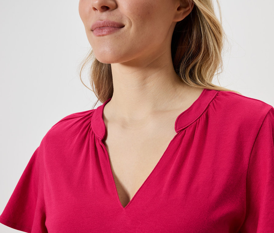 Gros plan d'une femme blonde portant un haut rose à col en V.