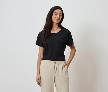 Femme portant un t-shirt noir et un pantalon beige, la main dans la poche.