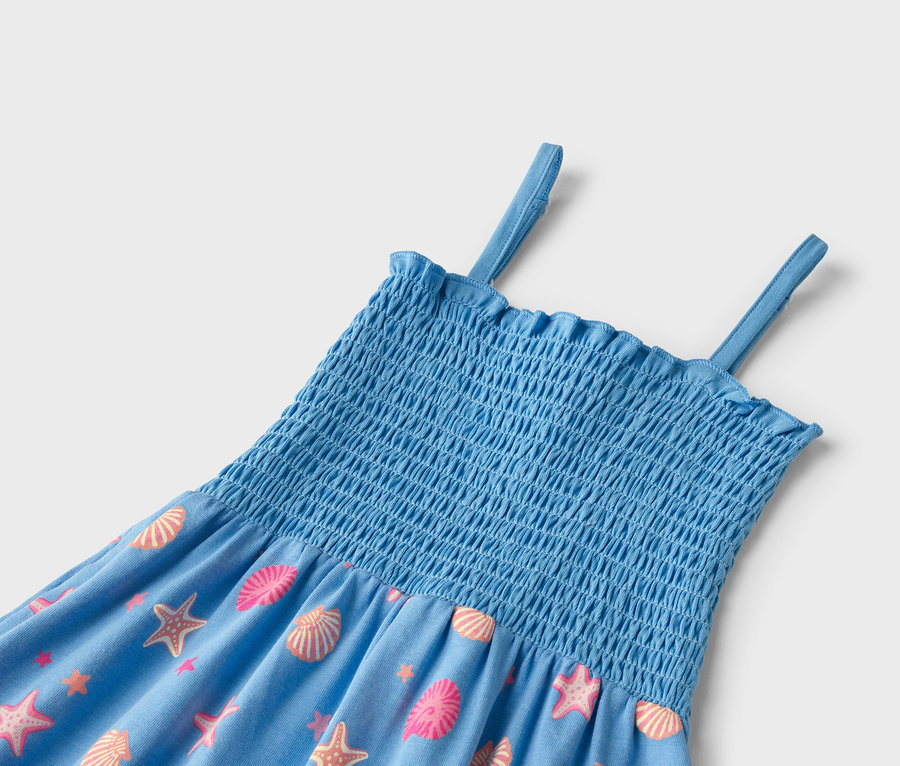 Gros plan sur une robe d'été bleue avec un haut élastique et des bretelles, imprimée de coquillages et d'étoiles de mer roses et orange.