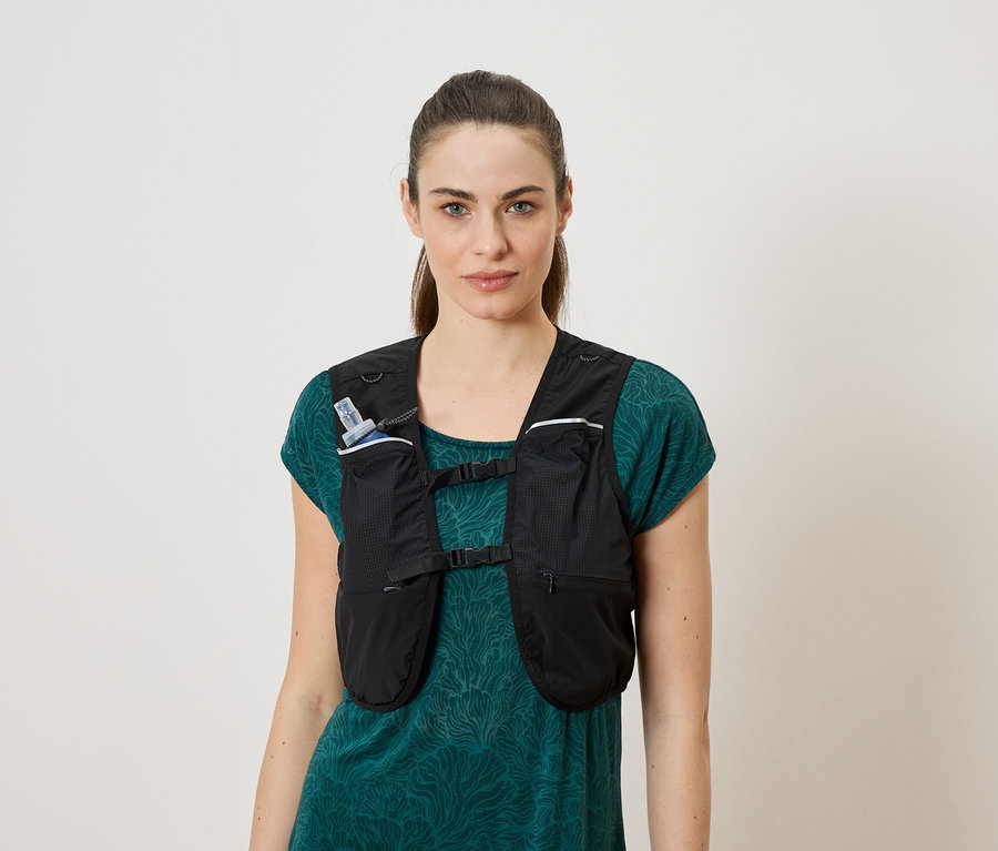 Femme portant un gilet de course noir sur un t-shirt bleu-vert. Une bouteille d'eau est rangée dans le gilet.